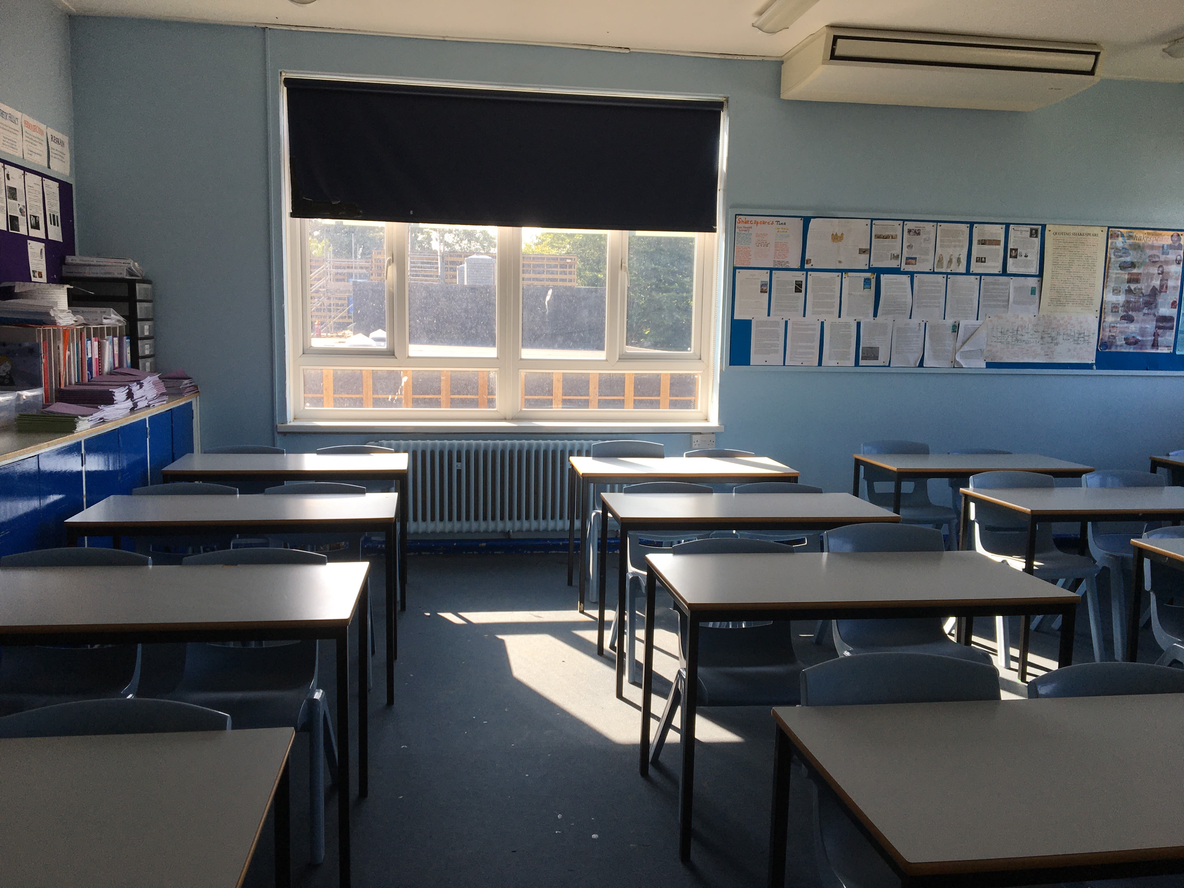 An empty classroom. Rows of tables and chairs and posters are on the wall.