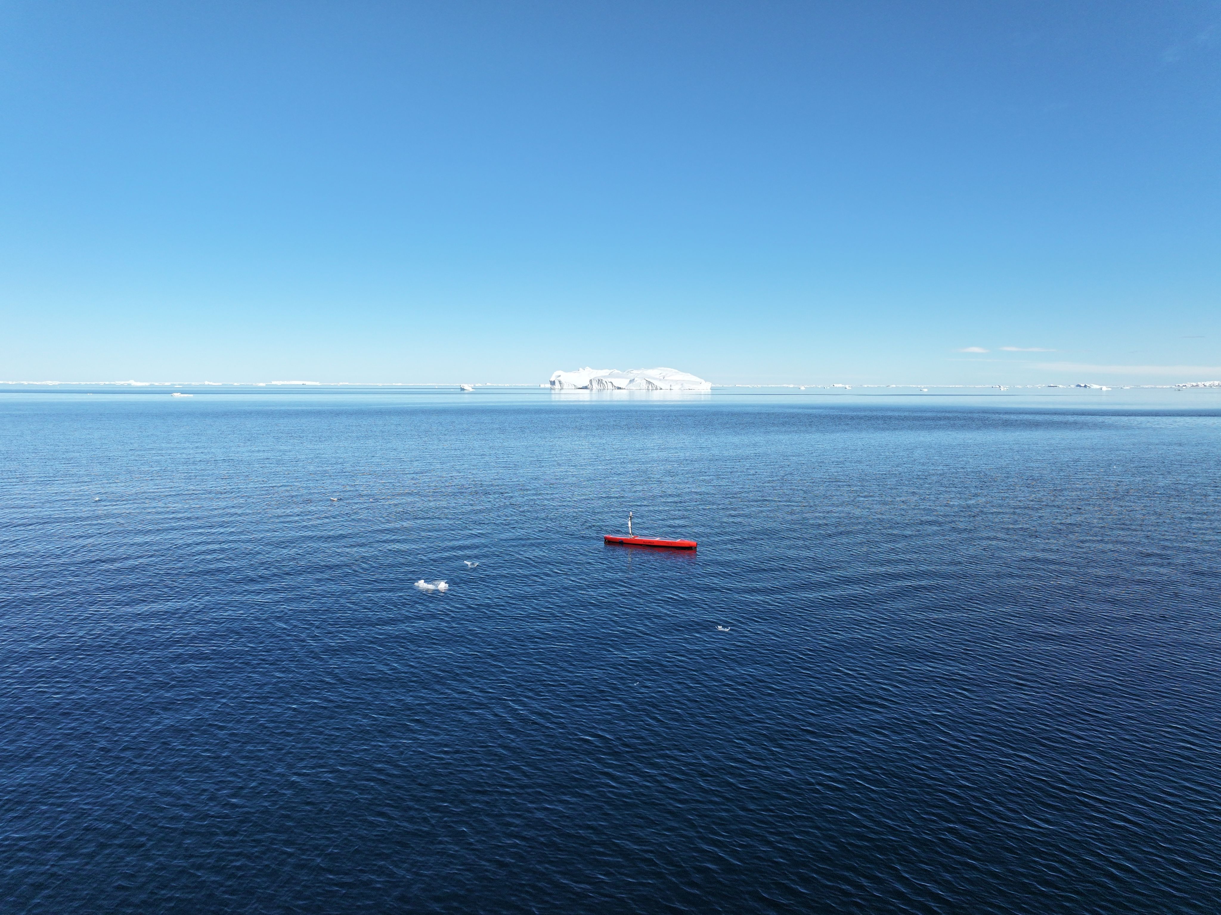 An autonomous surface vessel in the ocean with an iceberg in the distance.