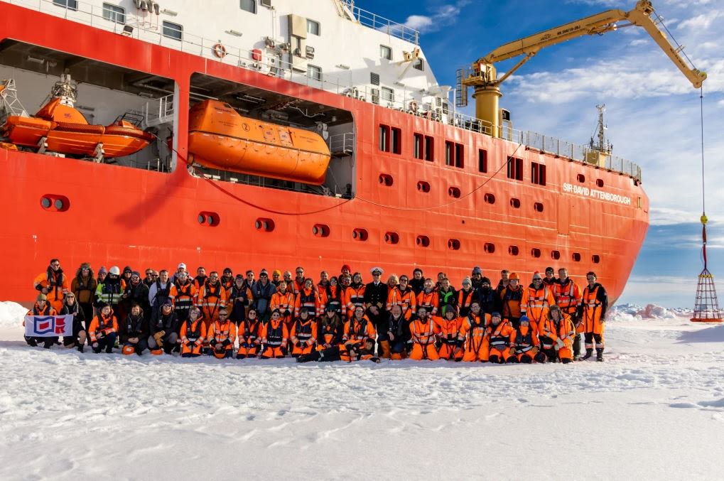 A group of people on snowy ice in front of a large red ship.