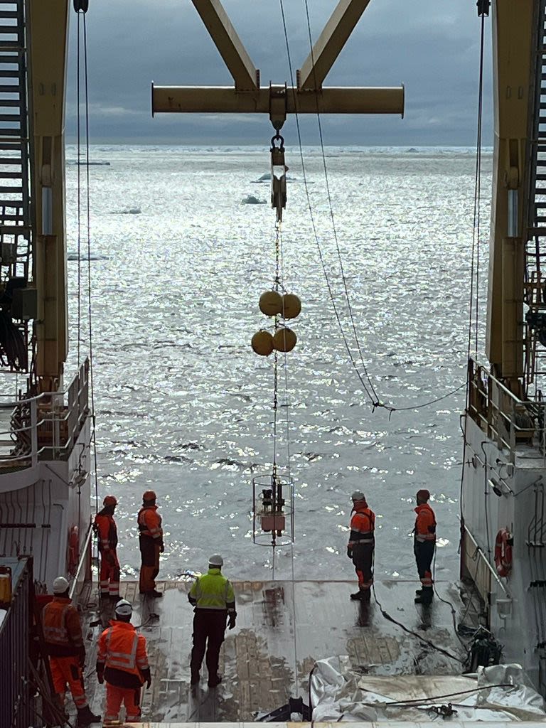 A crane lifting various scientific instruments containing bags of sea water.