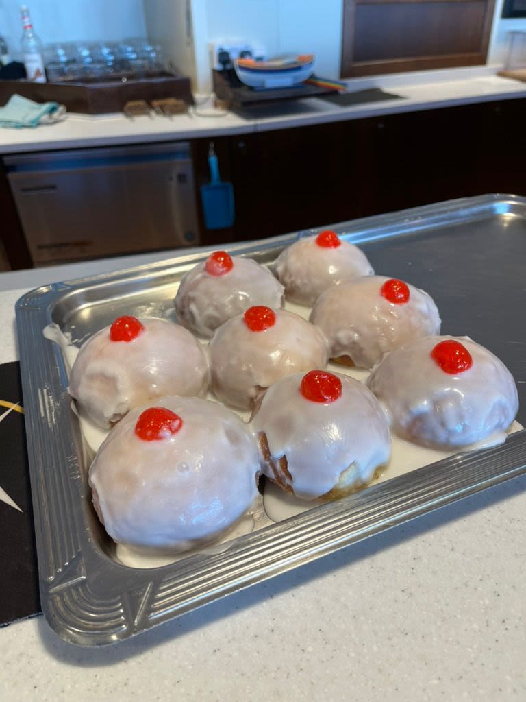 A 3 by 3 matrix of iced doughnuts on a tray, with one clearly already eaten from the top left.