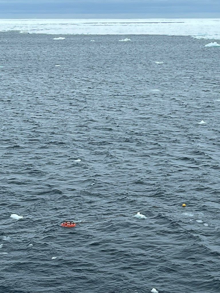 Amidst a big sea with ice in the background, a tiny orange spot on the bottom left indicates that the mooring has come up.